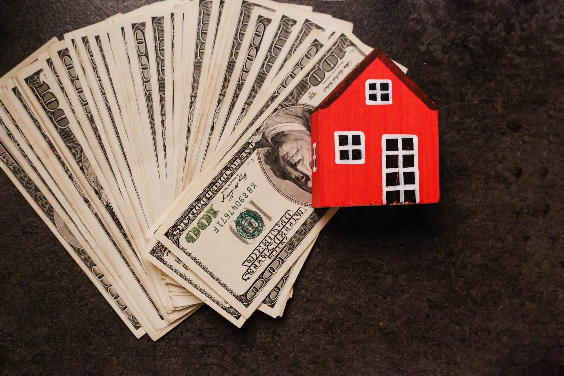 Red wooden house model over pile of money isolated on table background. Home money concept and free copy space.