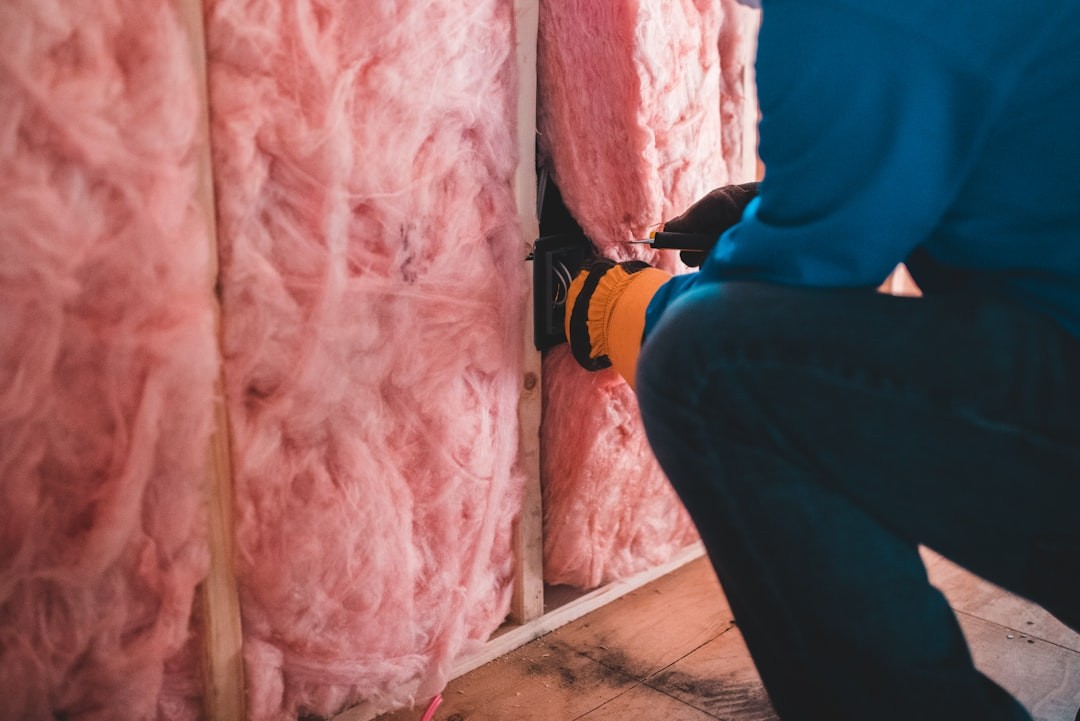 person installing pink insulation in between wooden studs